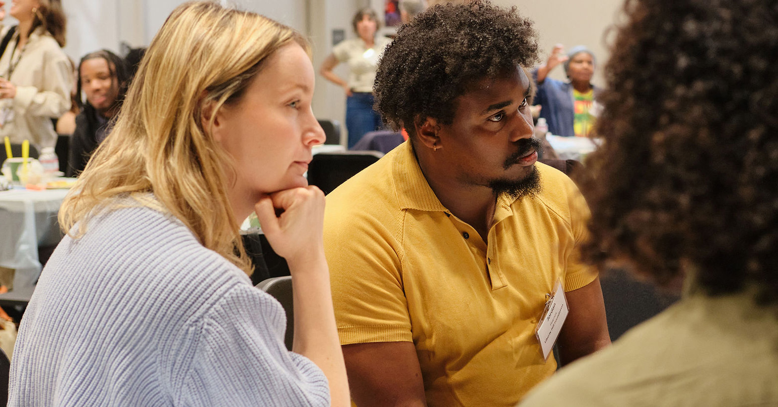 Image of a white woman and black man listening to someone off camera speak