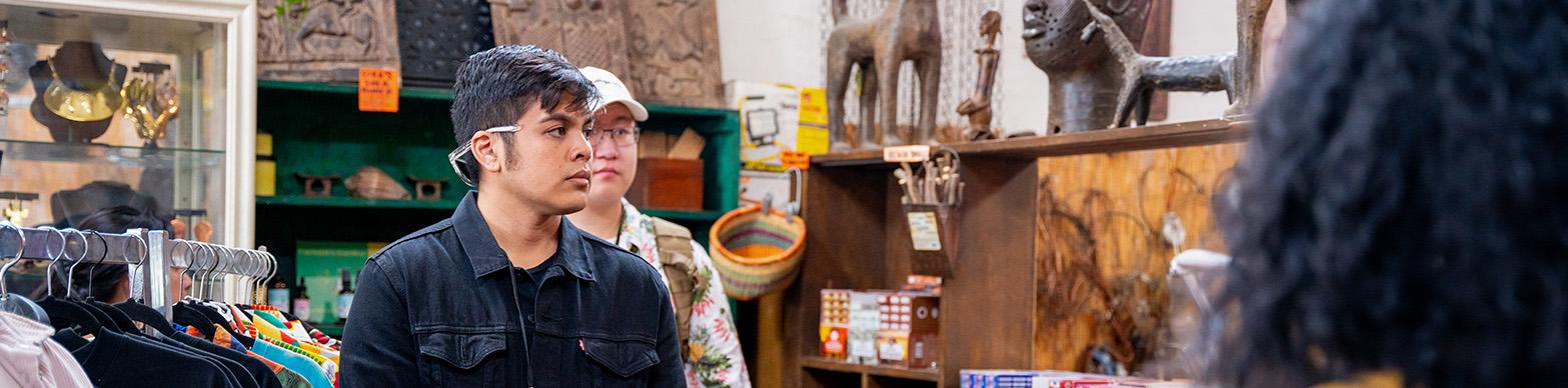 An interns stands in a workshop and listens to someone speak off camera