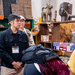 An interns stands in a workshop and listens to someone speak off camera