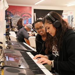 Two young women play piano together