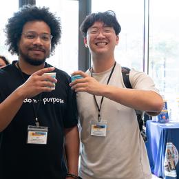 Two young men clink paper cups together as they pose for the camera
