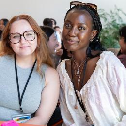 Two young women pose for a photo while sitting at a table