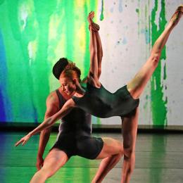 Two ballet dancers dance in front of a green and blue background